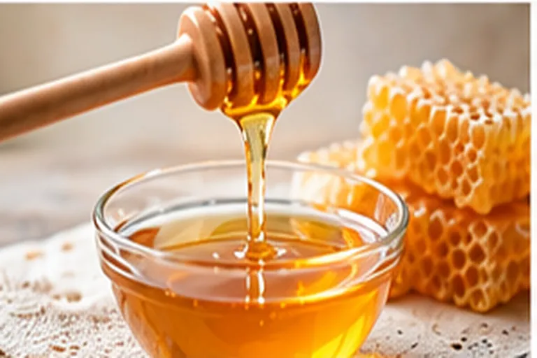 Golden honey pouring from a wooden dipper into a glass bowl beside pieces of honeycomb
